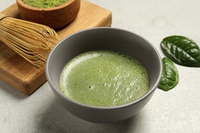 Photo of Cup of fresh green matcha tea and bamboo whisk on light grey table, closeup
