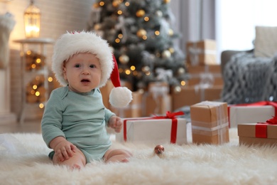 Image of Cute baby wearing Santa hat in room with Christmas tree