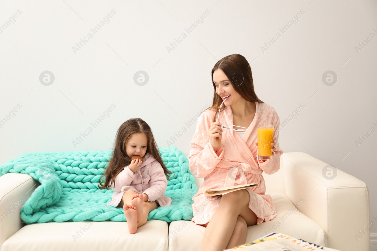 Photo of Mother and daughter in bathrobes sitting on sofa