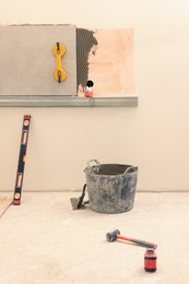 Photo of Adhesive mix with tile on wall and many different tools indoors