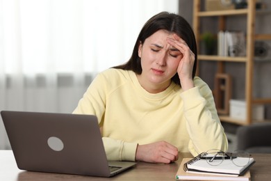 Overwhelmed woman sitting with laptop at table indoors