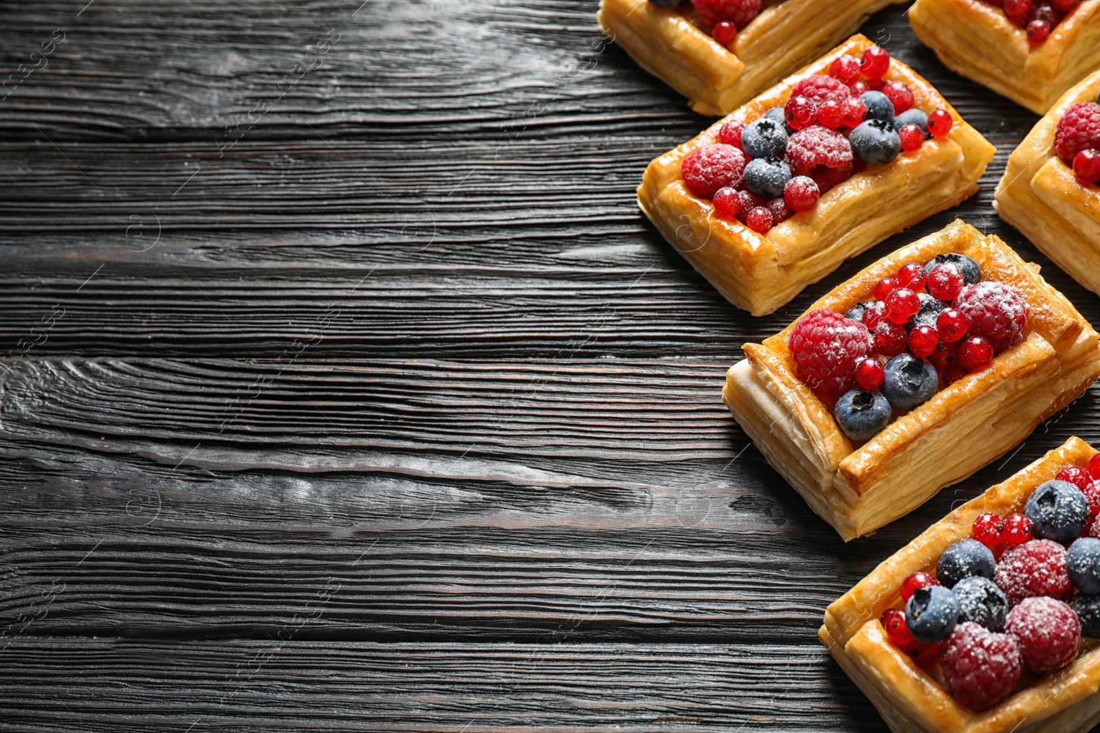 Photo of Fresh delicious puff pastry with sweet berries on dark wooden table. Space for text