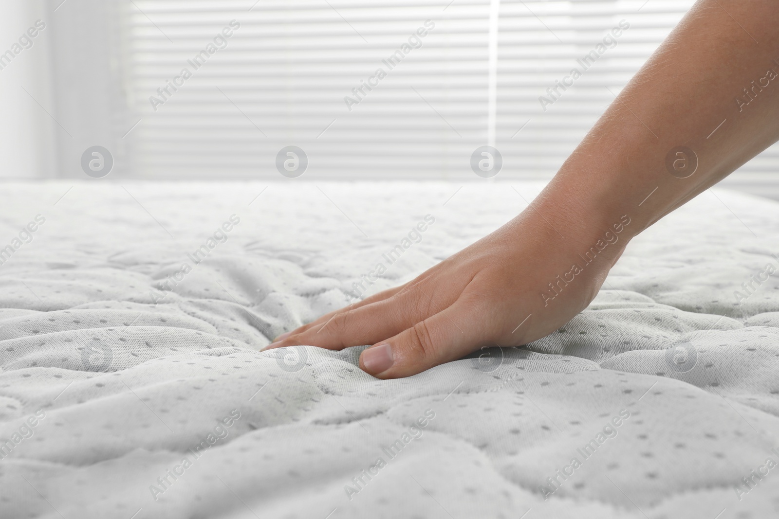 Photo of Woman touching soft light green mattress indoors, closeup