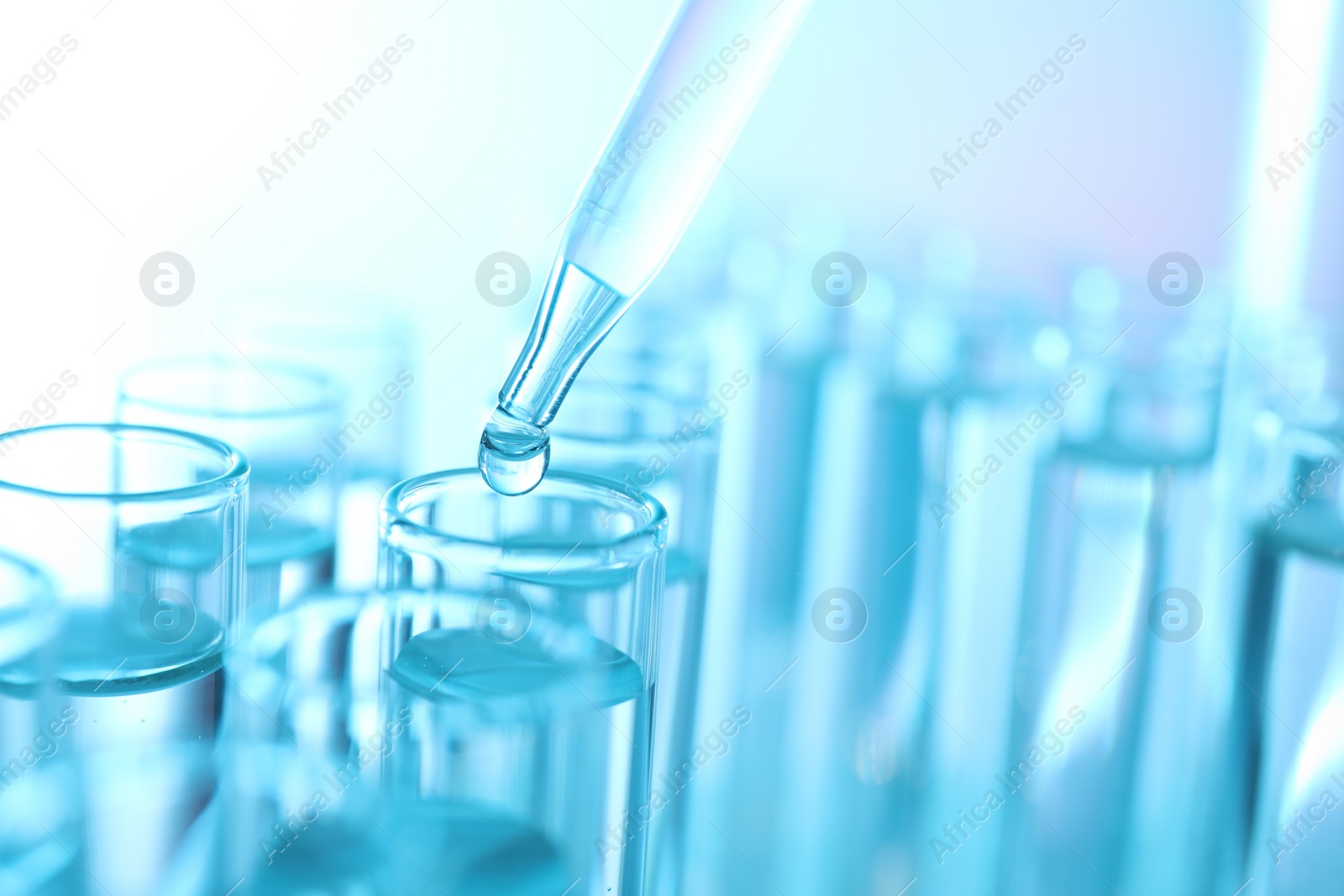 Photo of Dripping liquid from pipette into test tube on light blue background, closeup