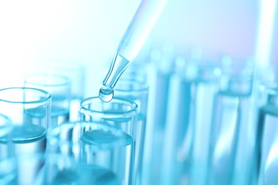 Photo of Dripping liquid from pipette into test tube on light blue background, closeup