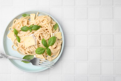 Photo of Delicious pasta with brie cheese, basil and fork on white tiled table, top view. Space for text
