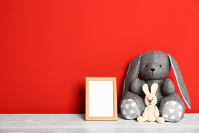 Photo of Soft toys and photo frame on table against red background, space for text. Child room interior