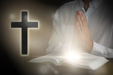 Man with Bible and cross praying at black table, closeup