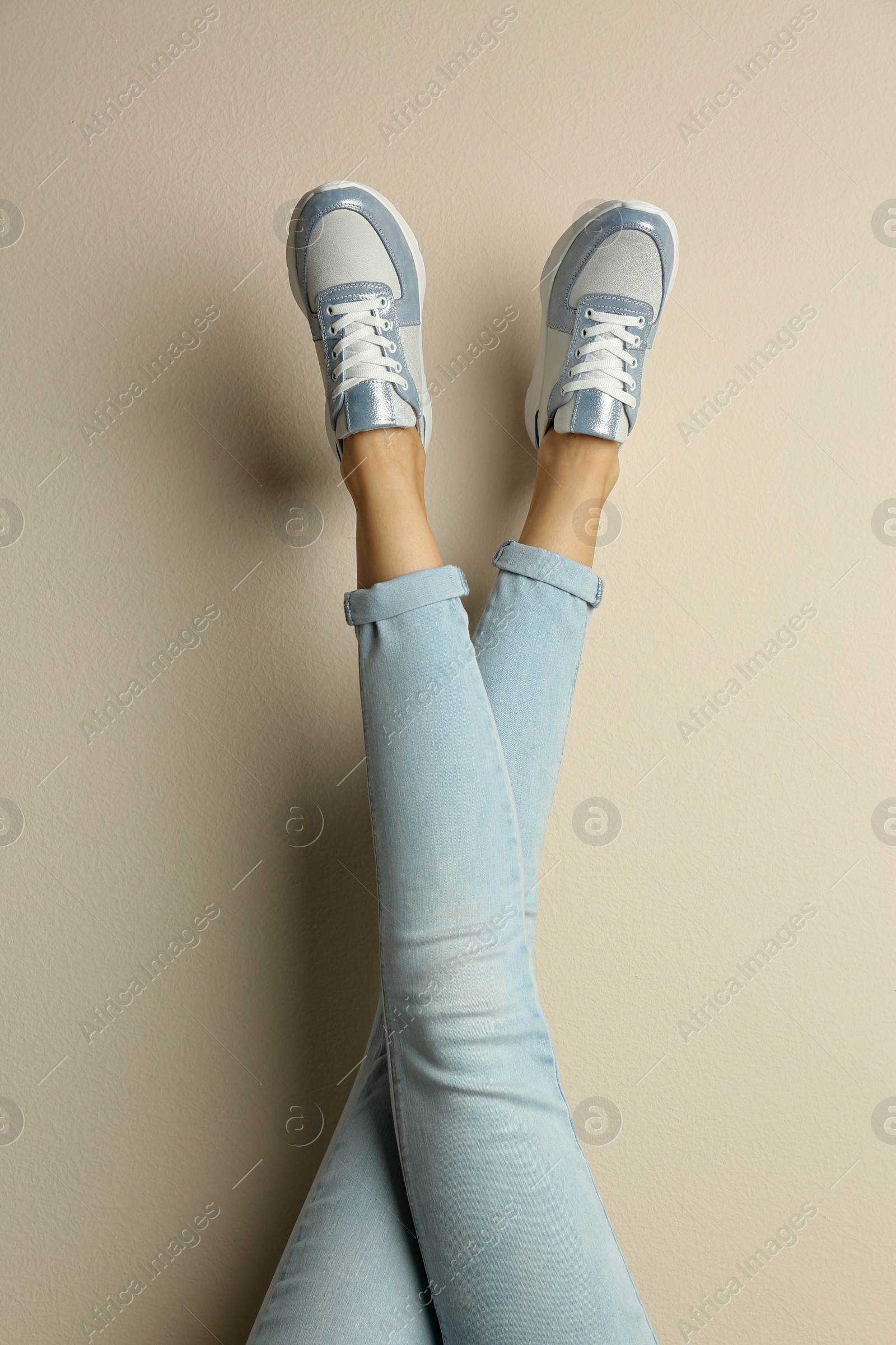 Photo of Woman wearing sneakers on beige background, closeup