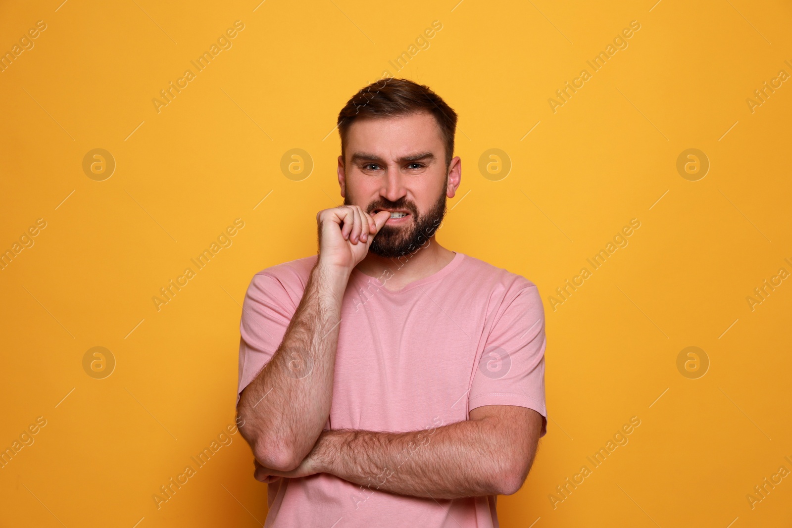 Photo of Man biting his nails on yellow background. Bad habit