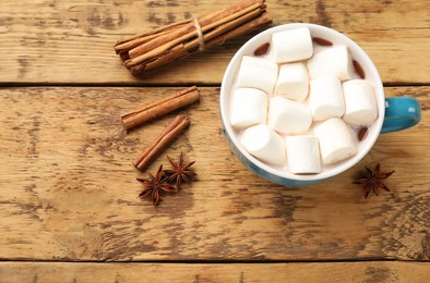 Photo of Tasty hot chocolate with marshmallows and spices on wooden table, flat lay. Space for text