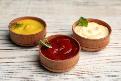 Photo of Bowls with mustard, ketchup and mayonnaise on wooden table, closeup