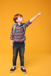 Photo of Cute schoolboy with backpack on orange background