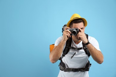 Male tourist with travel backpack taking picture on turquoise background, space for text