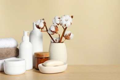 Photo of Different bath accessories and cotton flower on wooden table against beige background. Space for text