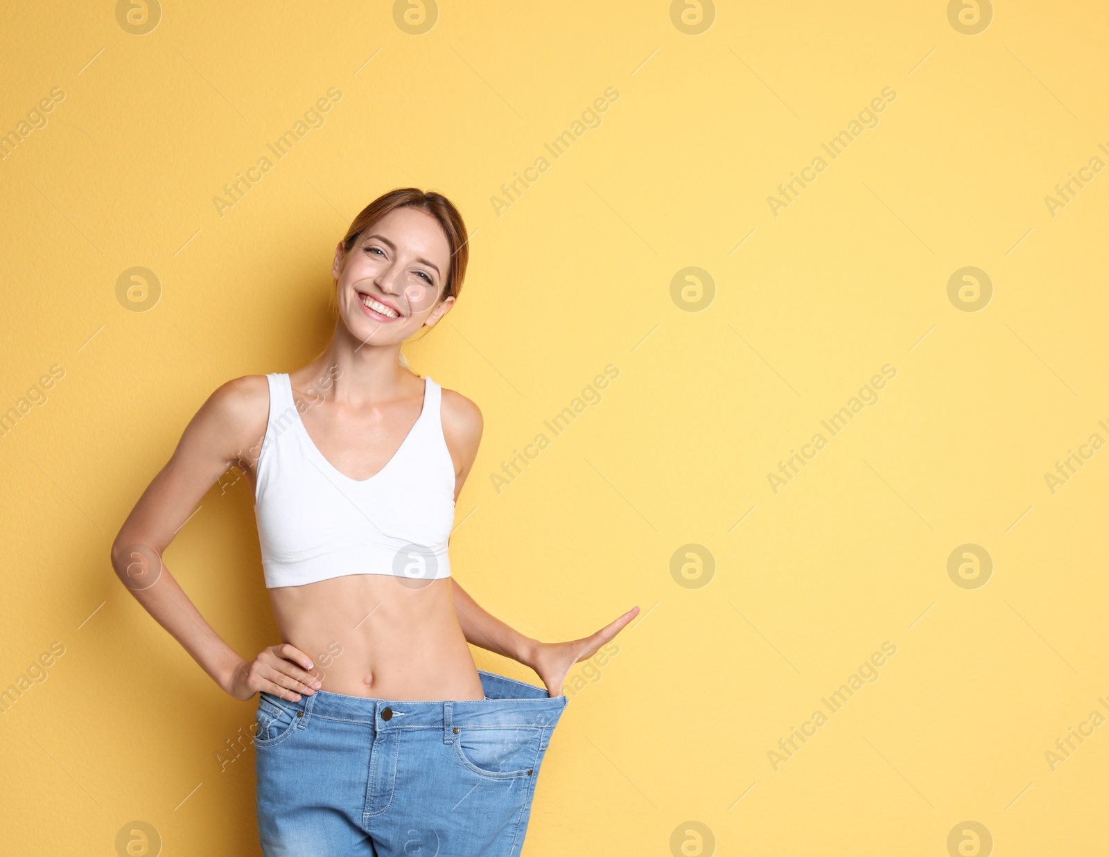 Photo of Young slim woman in old big jeans showing her diet results on color background