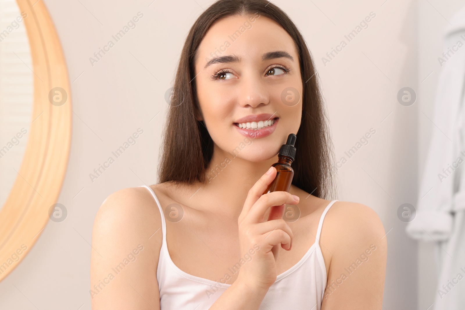 Photo of Young woman with bottle of essential oil in bathroom