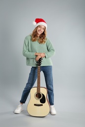 Photo of Young woman in Santa hat with acoustic guitar on light grey background. Christmas music