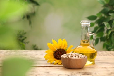 Photo of Sunflower, jug of oil and seeds on wooden table against blurred background, space for text