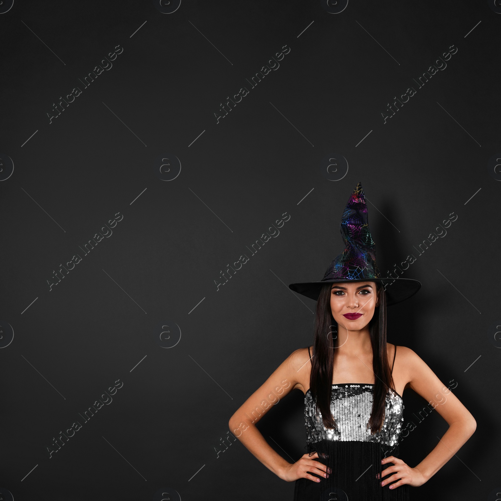 Photo of Beautiful woman wearing witch costume for Halloween party on black background, space for text