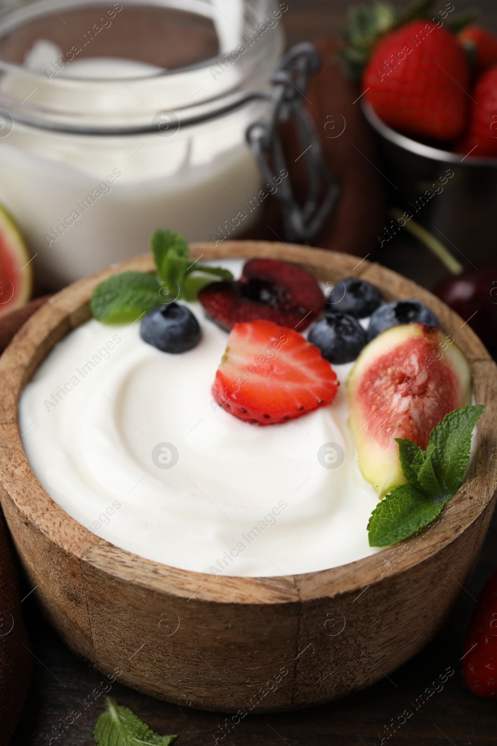 Photo of Bowl with yogurt, berries, fruits and mint on wooden table, closeup