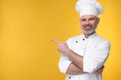 Photo of Happy chef in uniform pointing at something on orange background, space for text