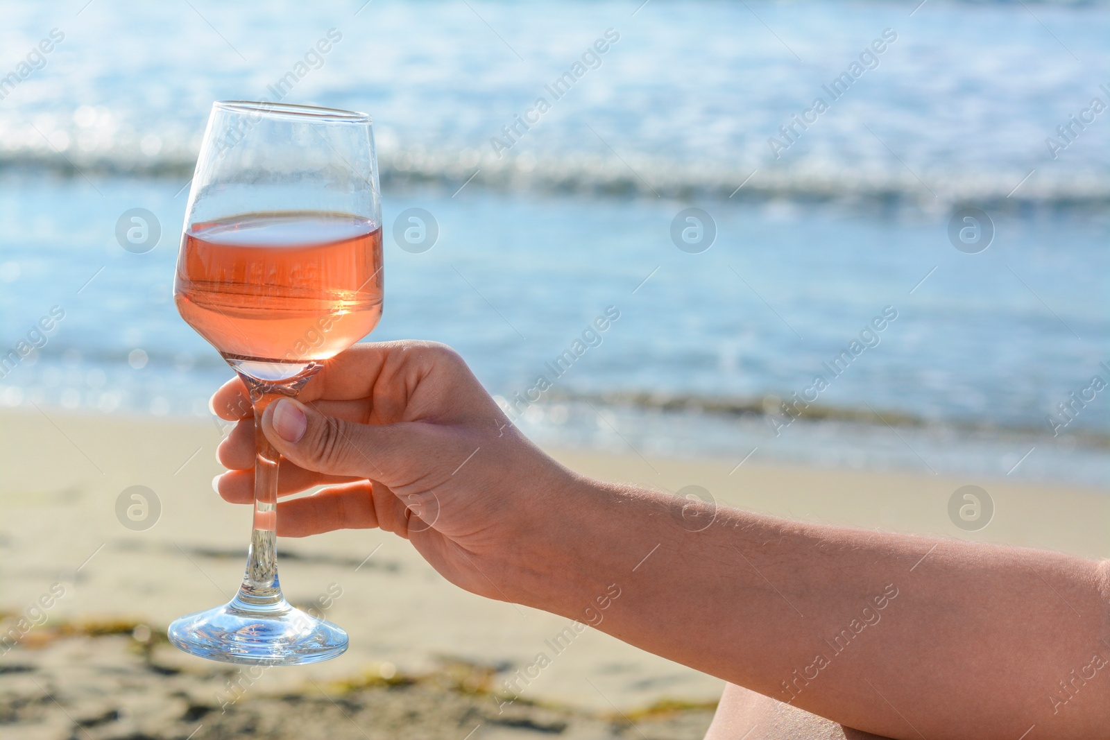 Photo of Woman with glass of tasty rose wine near sea, closeup