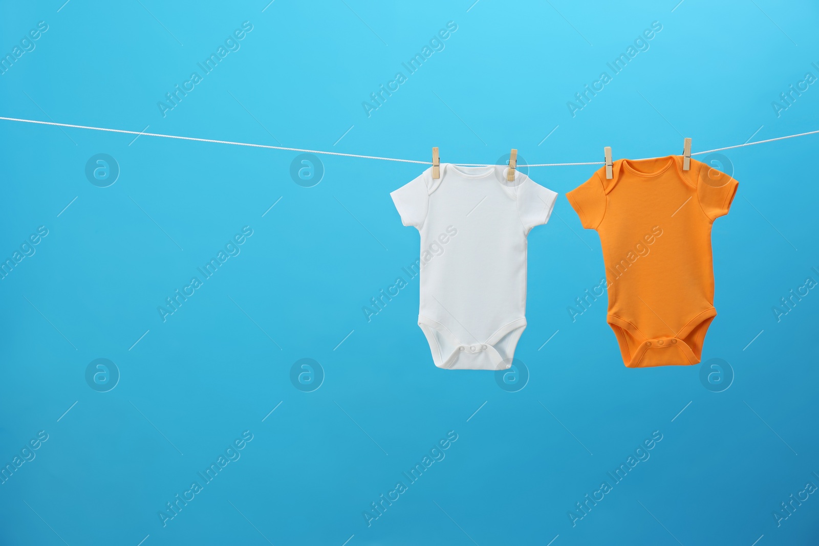 Photo of Colorful baby onesies hanging on clothes line against blue background, space for text. Laundry day