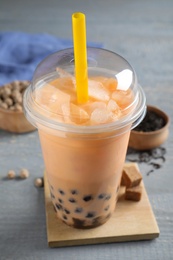 Tasty brown milk bubble tea in plastic cup on light blue wooden table, closeup