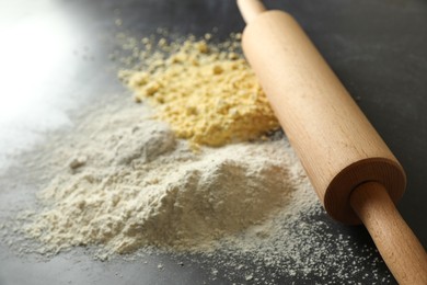 Rolling pin and different types of flour on black table, closeup