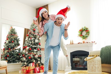 Photo of Happy couple in Santa hats near Christmas tree at home