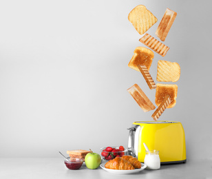 Image of Slices of grilled wheat bread flying out of toaster on light grey table 