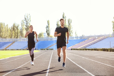 Sporty couple running at stadium on sunny morning