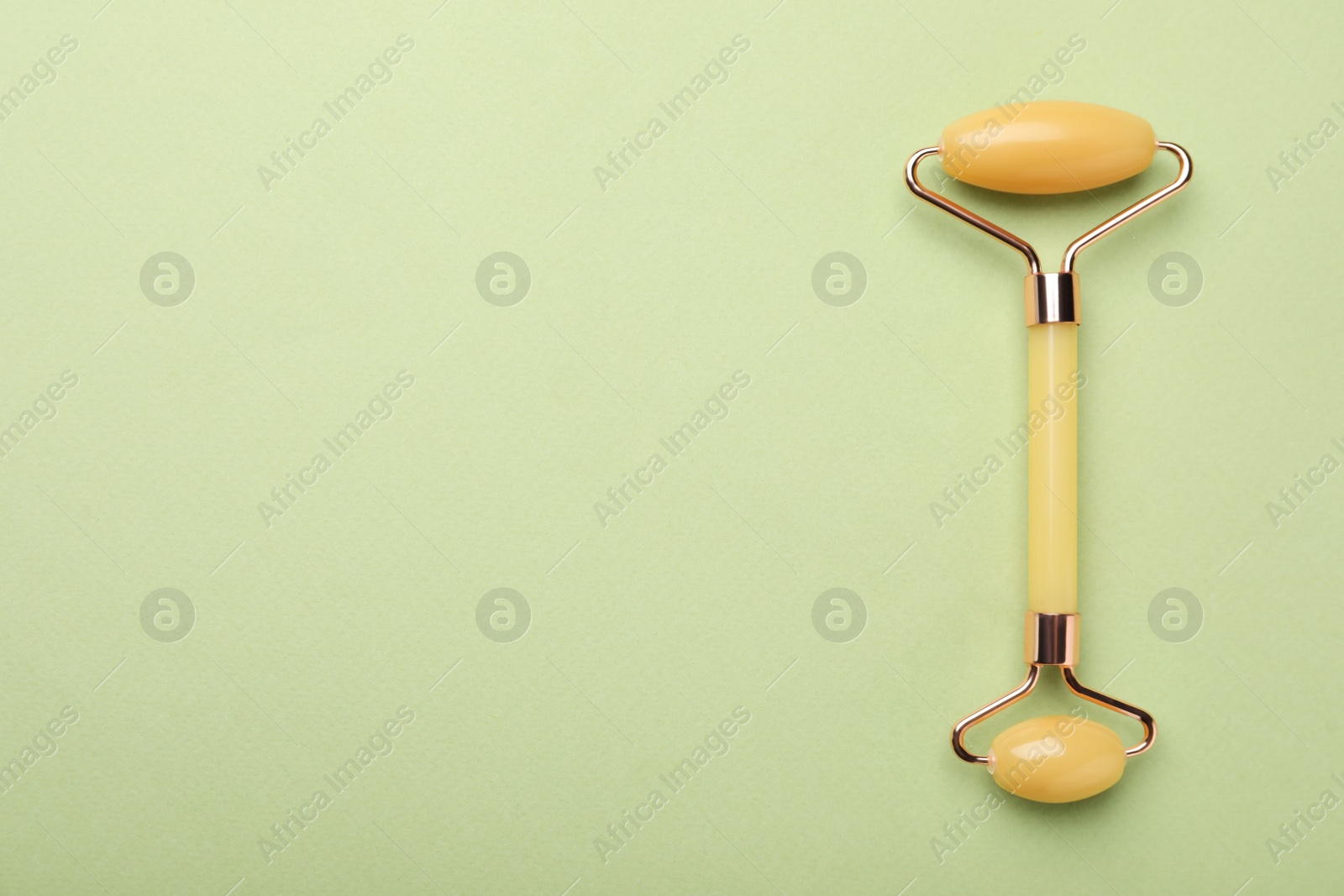 Photo of Natural face roller on green background, top view. Space for text
