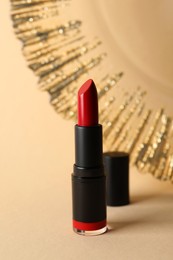 Photo of Beautiful glossy red lipstick on beige background