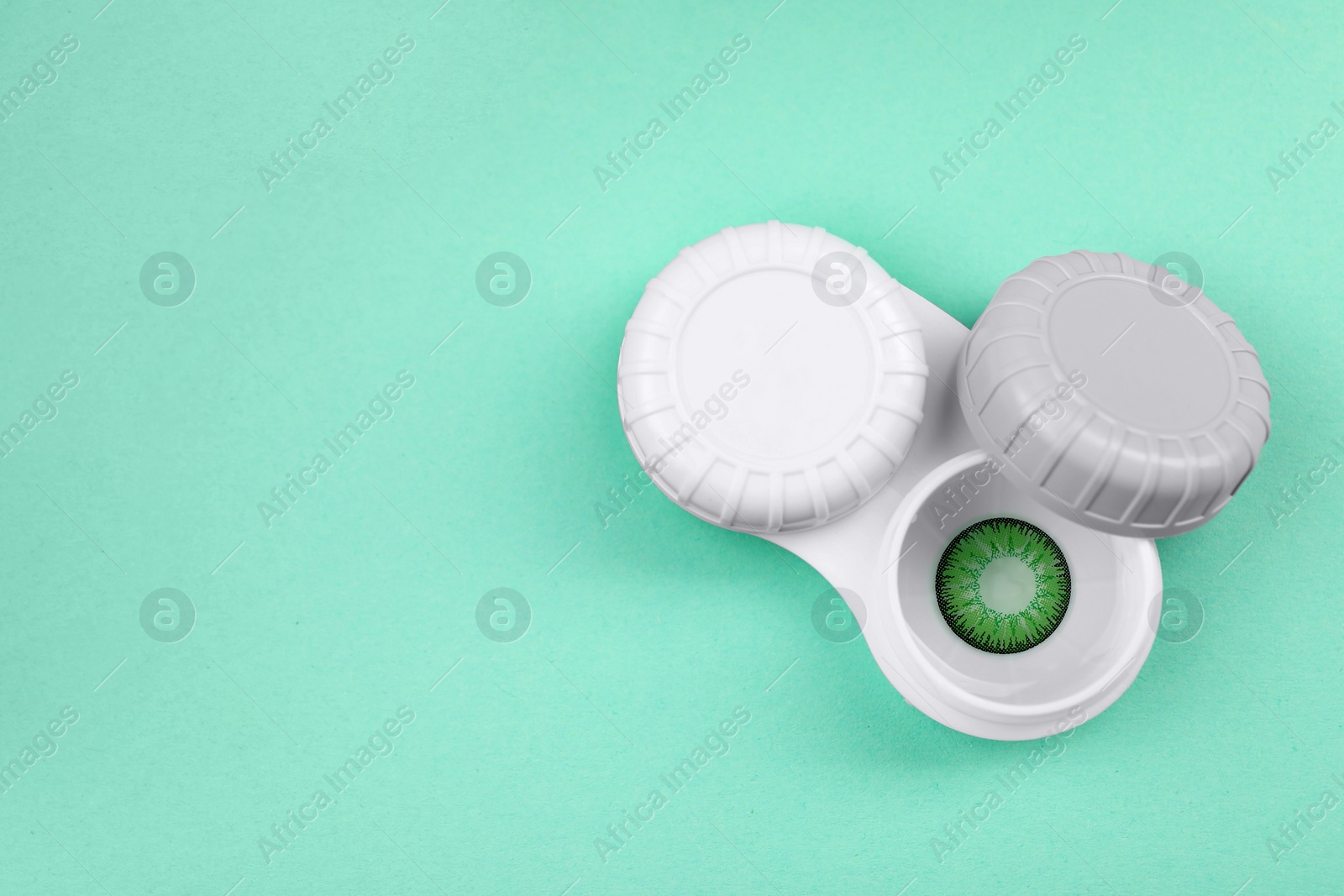 Photo of Case with green contact lenses on turquoise background, top view and space for text
