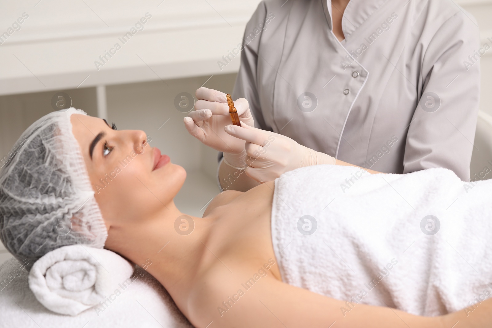 Photo of Professional cosmetologist holding skincare ampoule while working with client in clinic, closeup