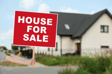 Image of House for sale. Woman holding signboard near beautiful house outdoors, closeup