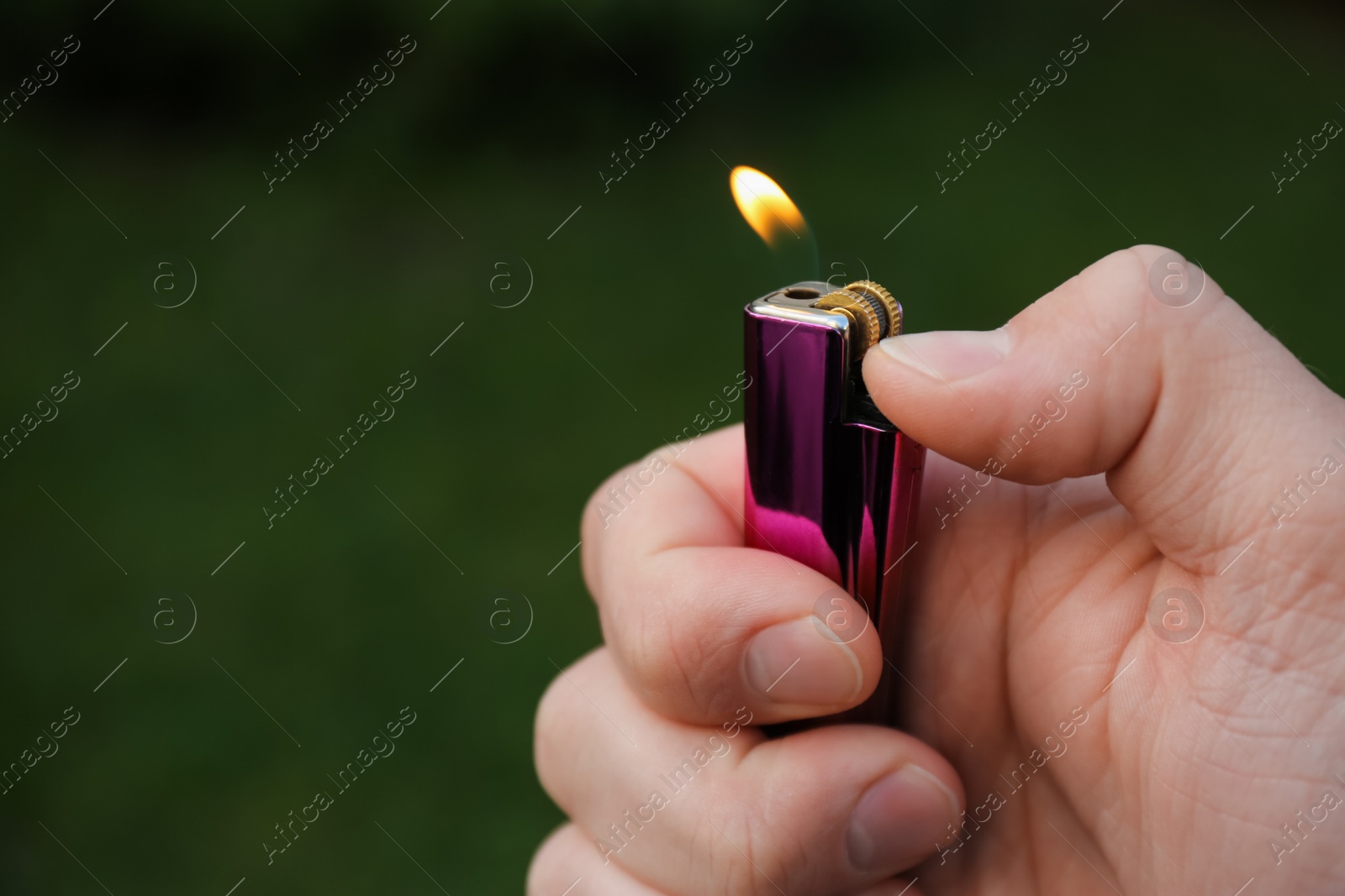 Photo of Man holding lighter with burning flame outdoors, closeup. Space for text