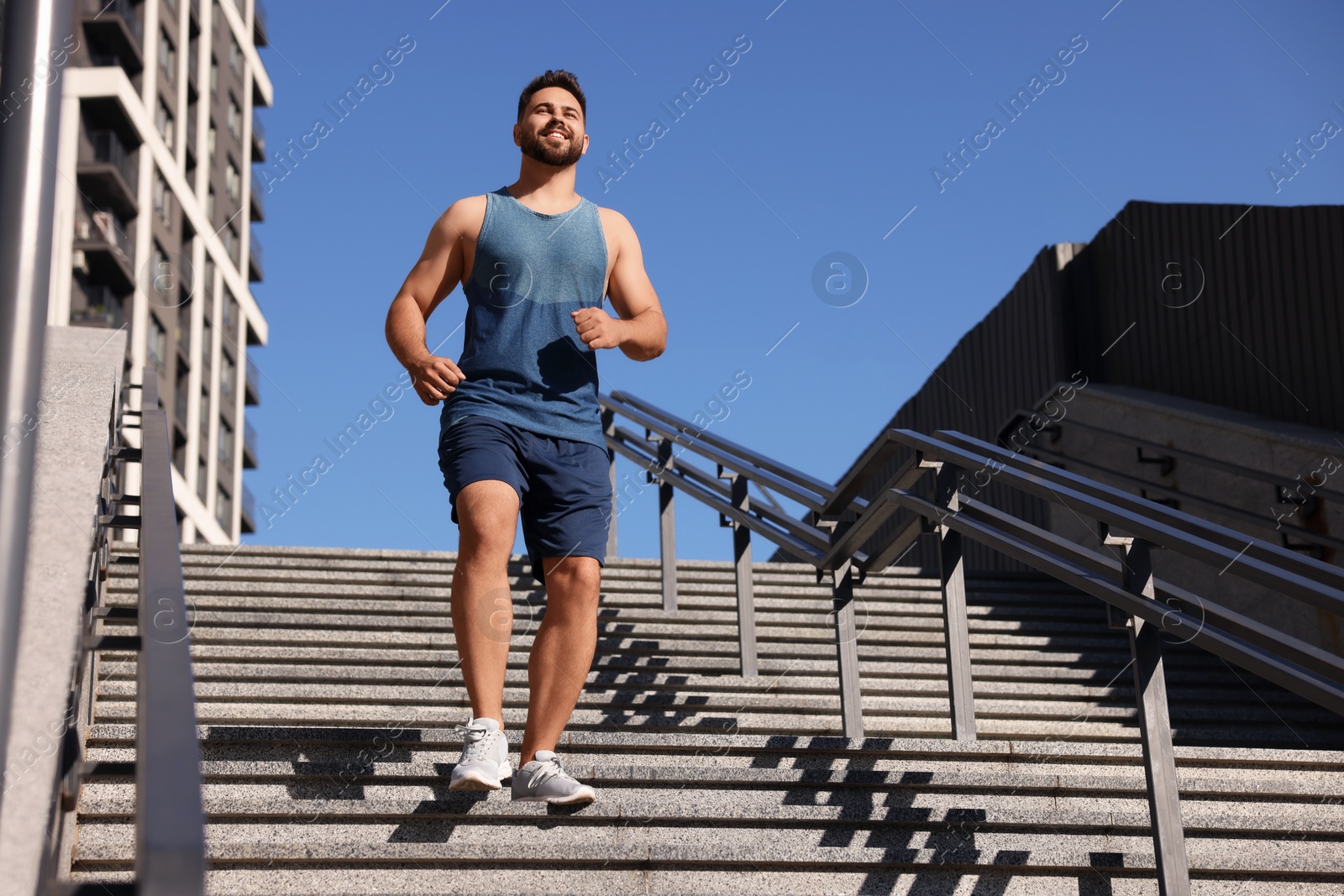 Photo of Happy man running down stairs outdoors on sunny day, low angle view. Space for text