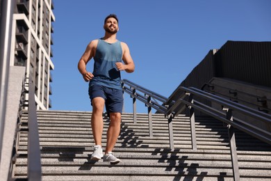 Happy man running down stairs outdoors on sunny day, low angle view. Space for text