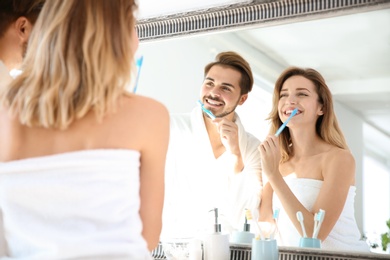 Photo of Young couple with toothbrushes near mirror in bathroom. Personal hygiene