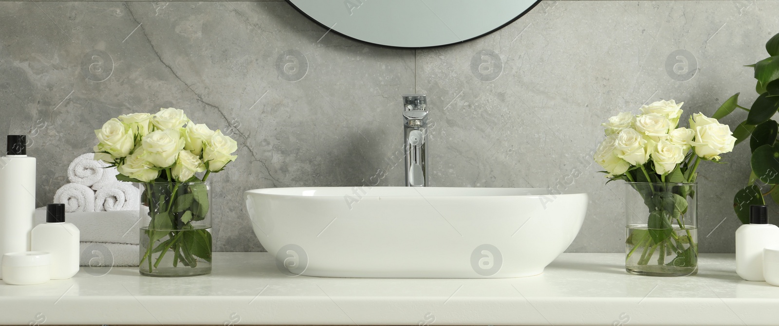 Photo of Beautiful roses and bath accessories near sink in bathroom