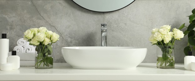 Photo of Beautiful roses and bath accessories near sink in bathroom