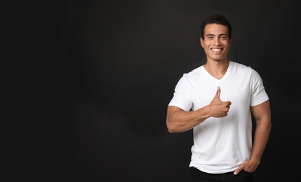 Photo of Handsome young African-American man showing thumbs-up gesture on black background