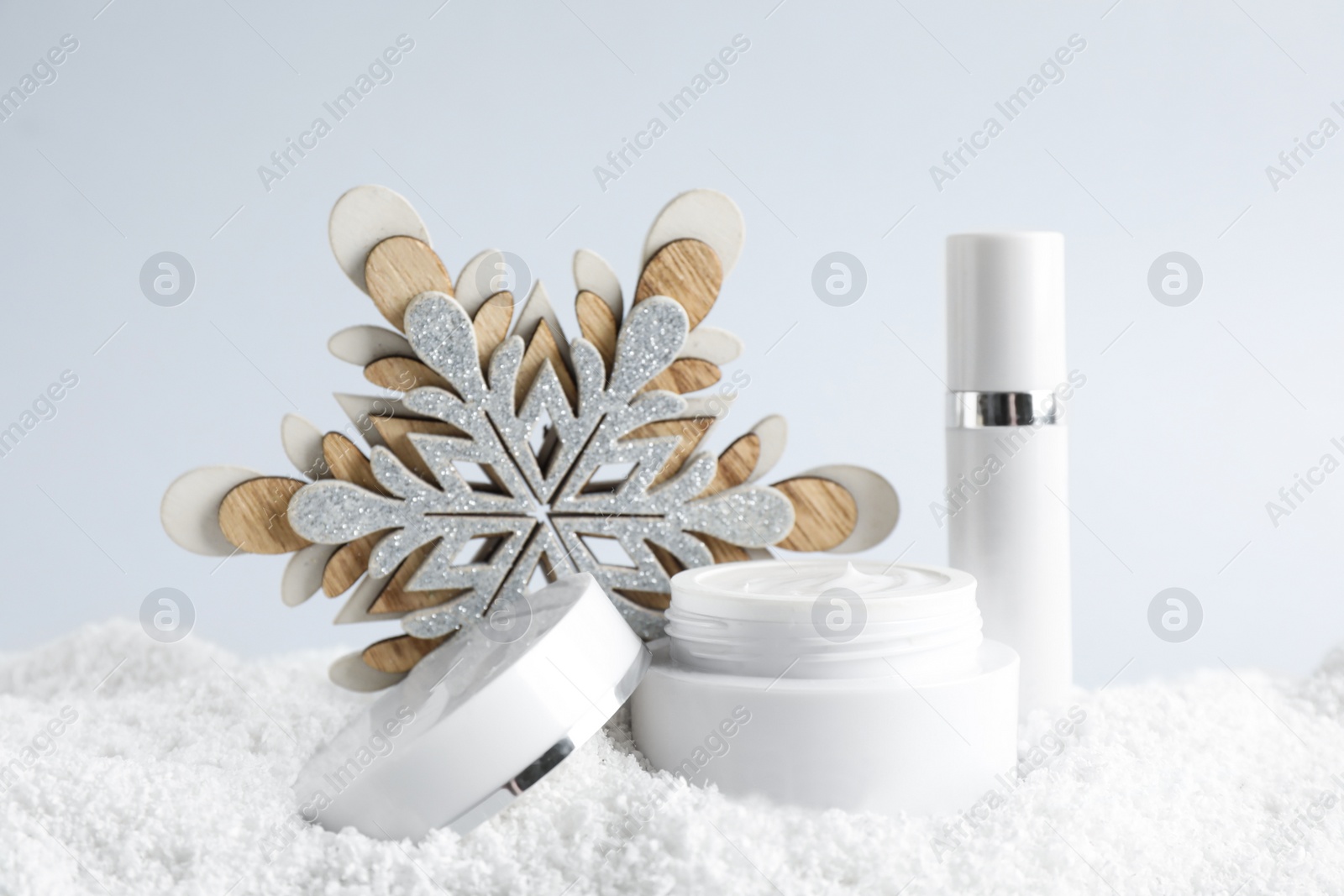 Photo of Jar of hand cream and lip balm near decorative snowflake on snow against light background. Winter skin care cosmetics