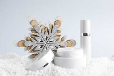 Photo of Jar of hand cream and lip balm near decorative snowflake on snow against light background. Winter skin care cosmetics