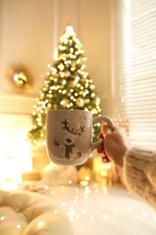 Photo of Woman with cup of drink and blurred Christmas tree on background, closeup