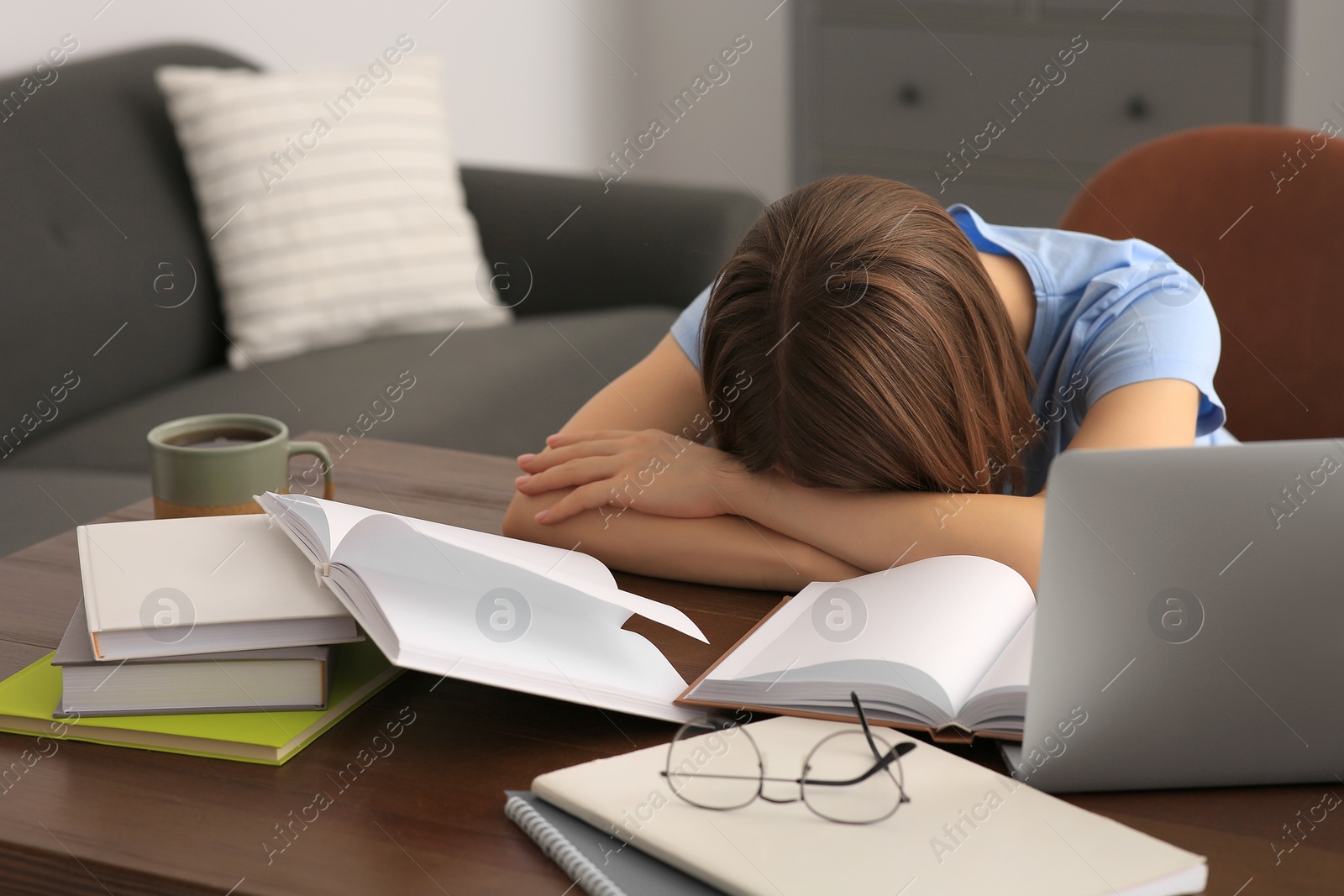 Photo of Young tired woman sleeping near books at wooden table indoors