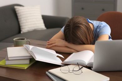 Young tired woman sleeping near books at wooden table indoors